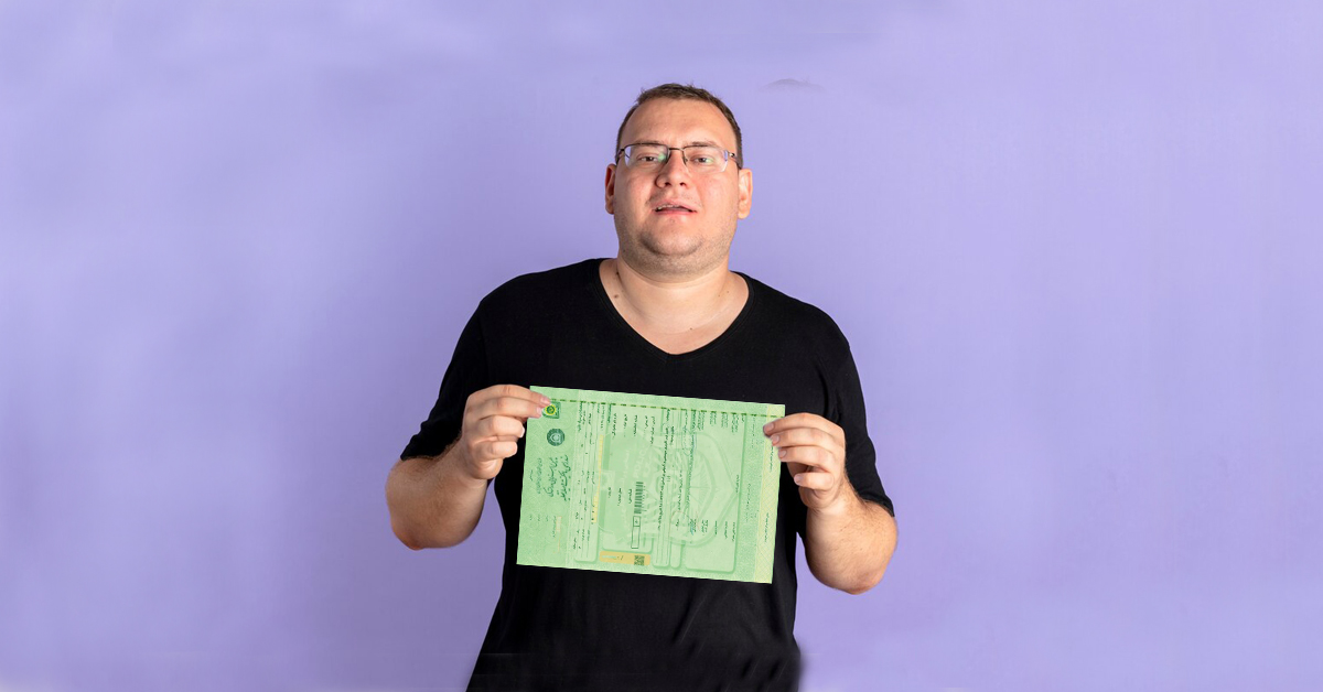 A replica of a green leaf is in the hands of a man with low back hair and a black blouse